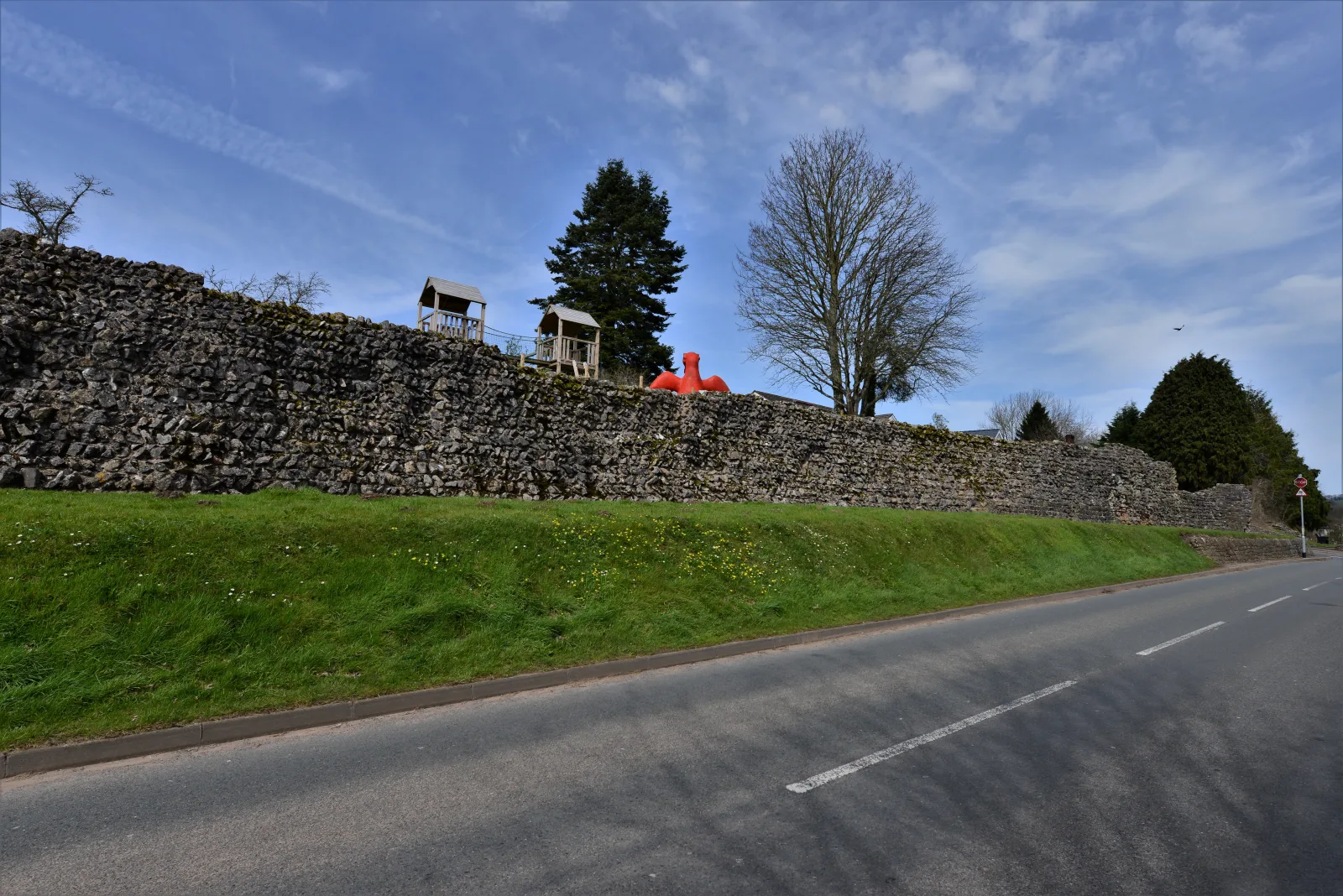 A long surviving section of Caerwent's Roman stone town wall beside a modern road and village.