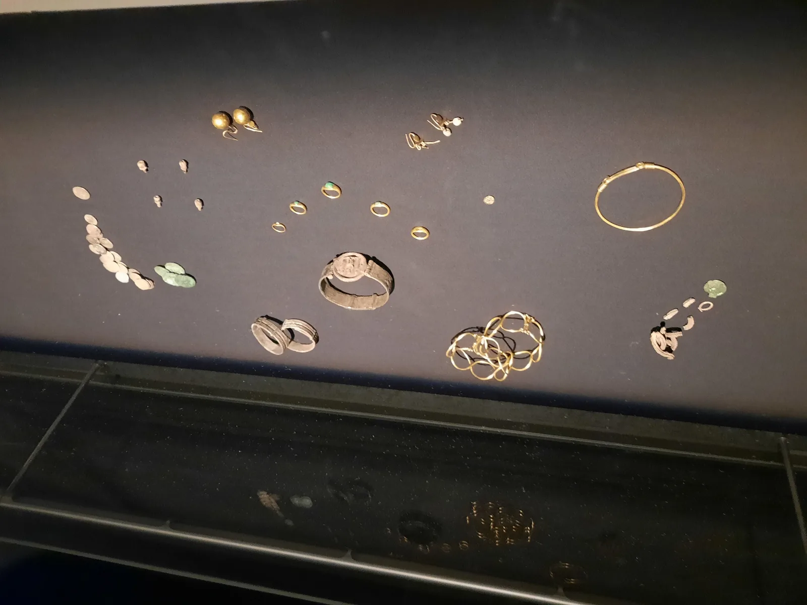 Roman gold and silver jewellery, coins and personal objects displayed against a dark background.